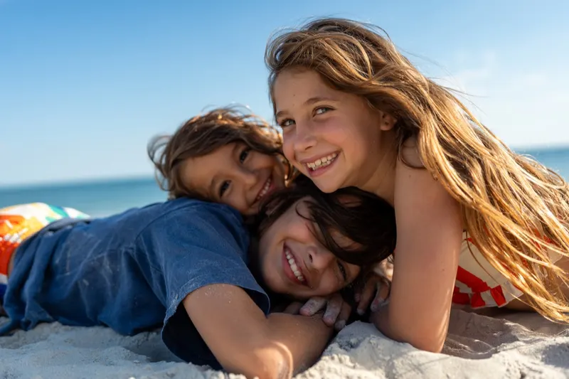 Three smiling children lying together on the sand on a beach vacation