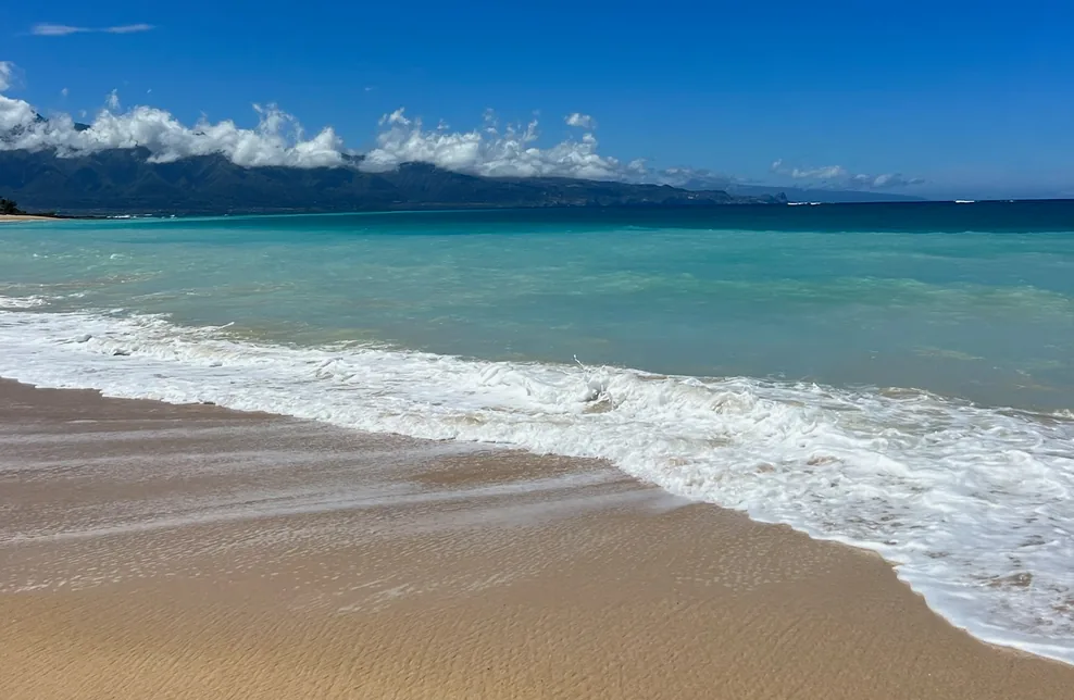 Calm turquoise water and golden sand on a Maui beach with the West Maui mountains behind